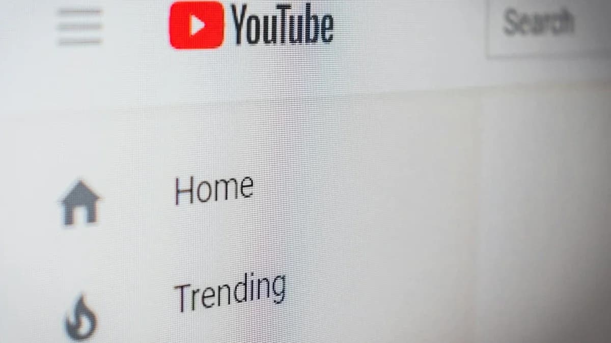YouTube YouTube app interface com aba Inscrições na barra inferior: Tela de computador com logotipo do YouTube e menu Home e Trending em close, fundo desfocado.