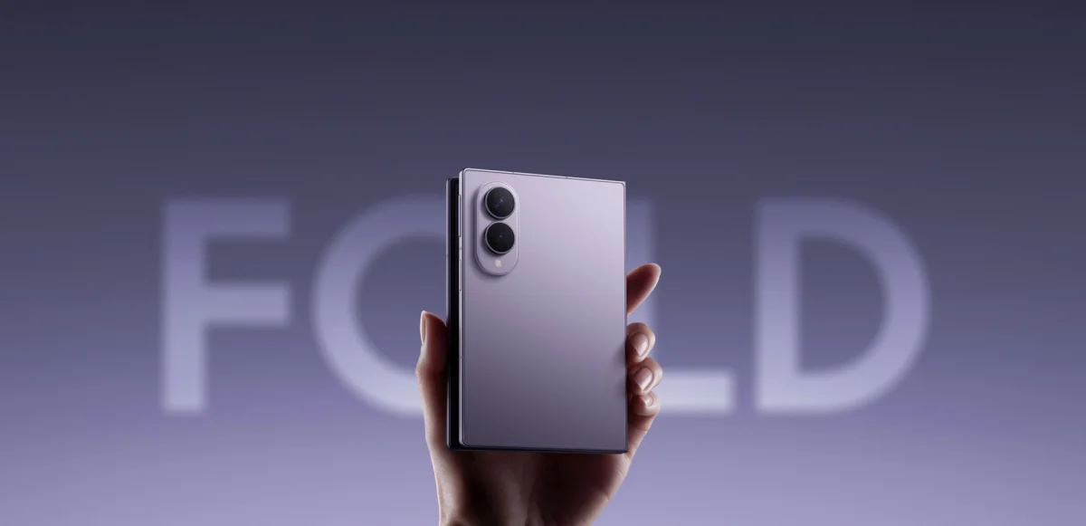 Samsung Galaxy Z Fold8: Aparelho dobrado na vertical, cor lilás, com duas câmeras traseiras, segurado por uma mão em fundo lilás com a palavra FOLD desfocada.