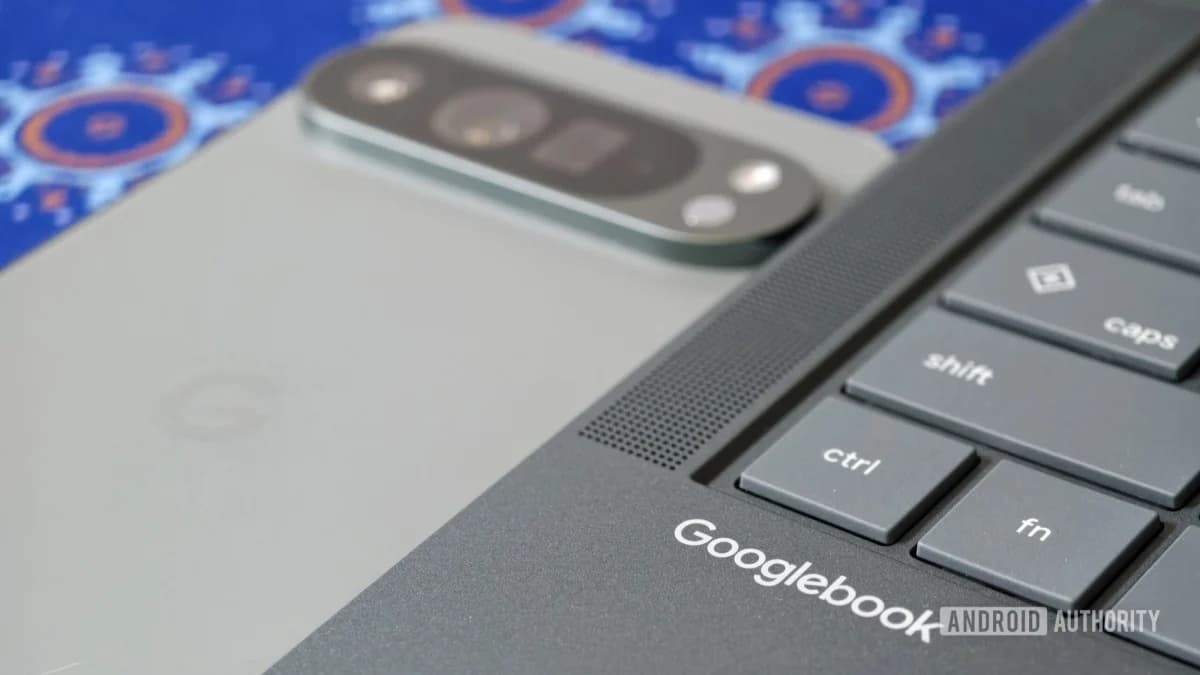 HP Googlebook 14: Close-up do teclado e da borda de um notebook Googlebook escuro, com a marca escrita, ao lado da traseira clara de um celular.
