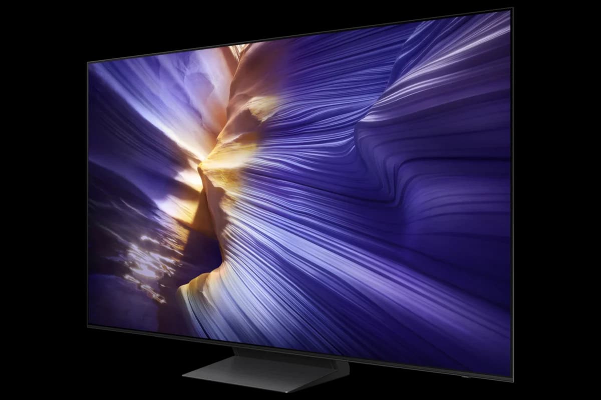 Samsung OLED S90F: Televisor de tela OLED preto com a tela mostrando um padrão de ondas roxas e douradas, visto de lado sobre base escura, em fundo cinza claro.