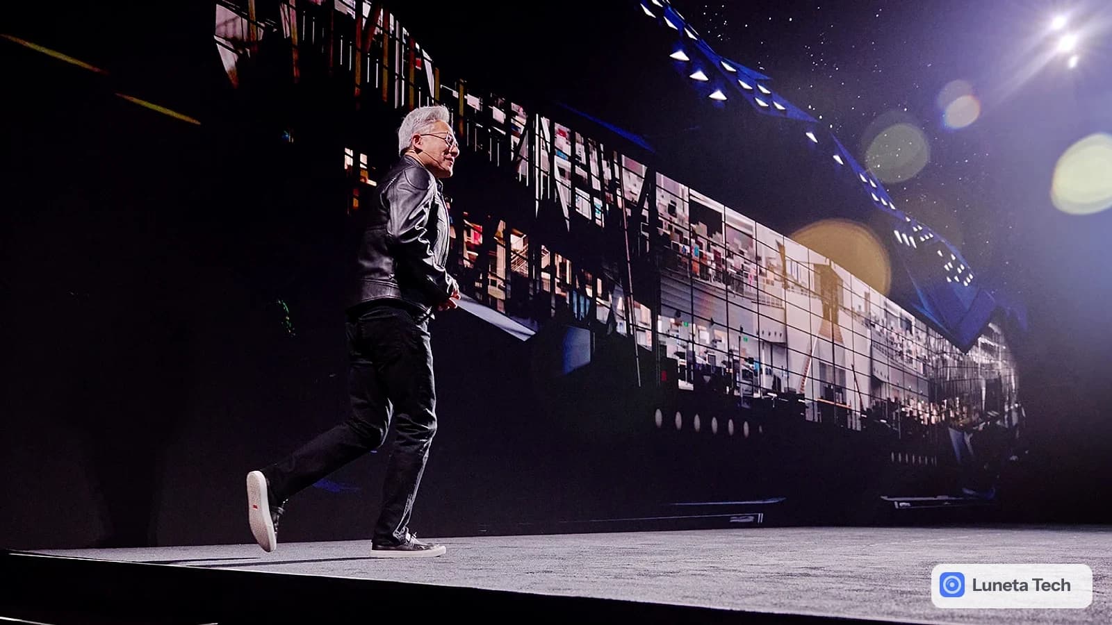 NVIDIA GTC Berlin, conferência de tecnologia da NVIDIA: Homem de jaqueta de couro preta caminhando em palco escuro, de costas para a plateia, com telão grande a