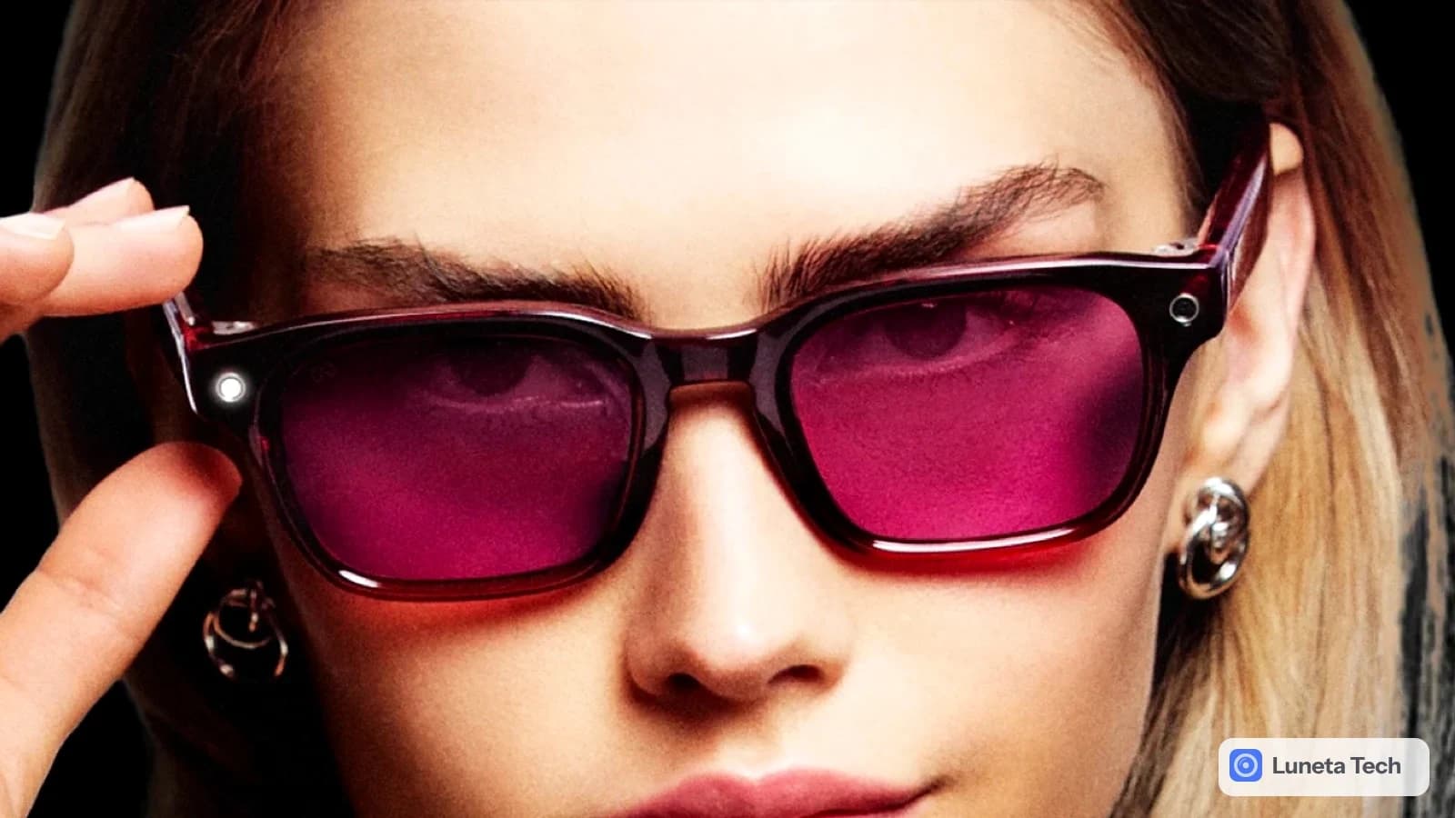 Ray-Ban Meta Gen 3: Modelo de cabelo castanho segurando com a mão a armação de óculos de sol vinho-avermelhado, fundo preto, vista de frente em close.