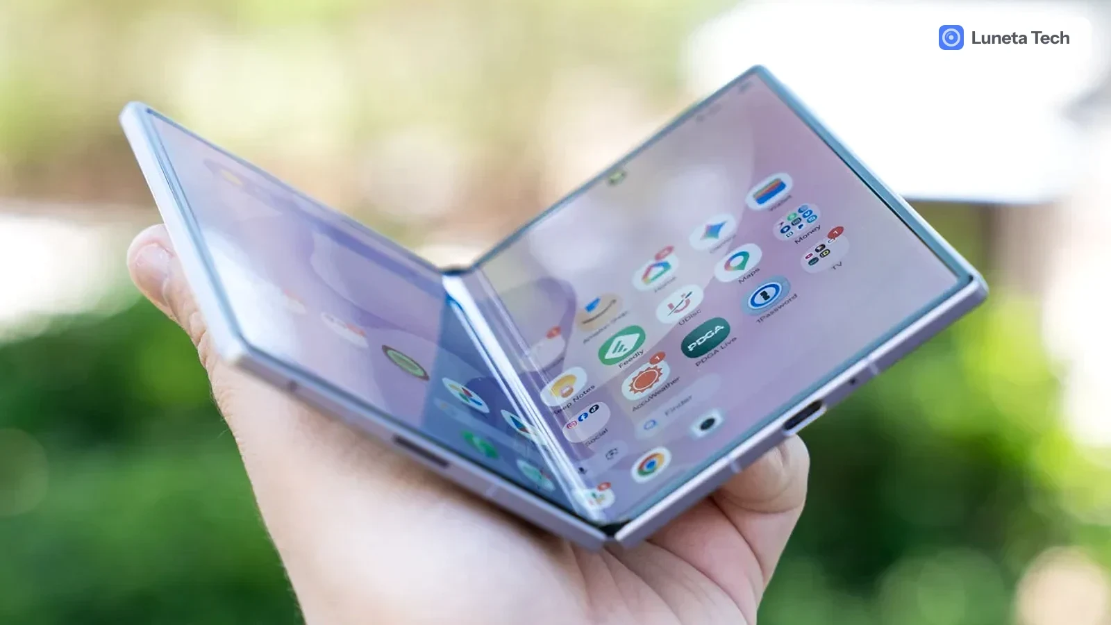 Samsung Galaxy Z Fold 8: Smartphone dobrável semiaberto, de cor prateada, segurado por uma mão ao ar livre, com a tela inicial cheia de aplicativos visível.