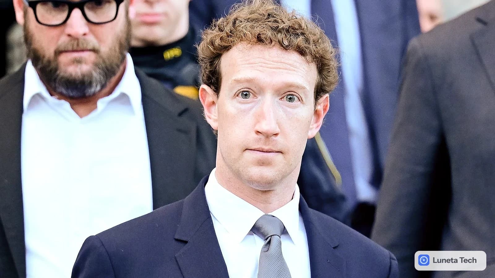 Meta, Facebook, processo de privacidade no Novo México: Homem de terno escuro e gravata cinza saindo de um prédio, cercado por seguranças, olhar sério para a câ