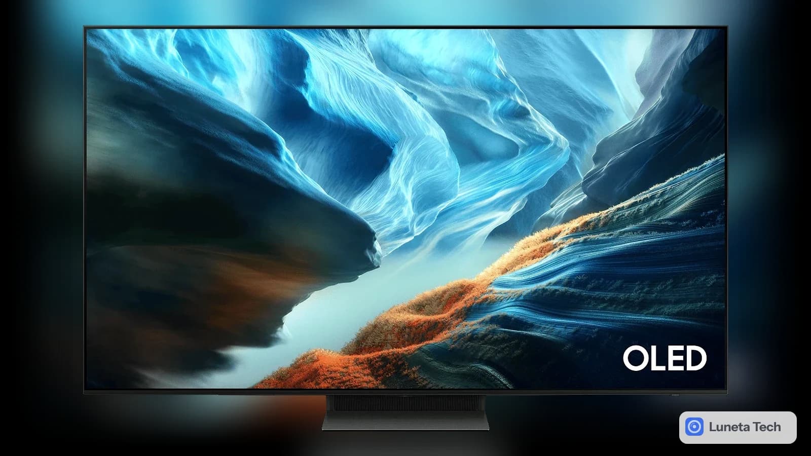Samsung OLED S90H: Televisor OLED de moldura fina e base central escura, de frente, com tela exibindo paisagem azul e laranja, sobre fundo cinza-azulado claro.