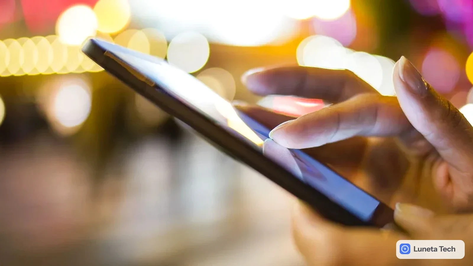 Phishing golpe de encomenda SMS: Mãos tocando a tela de celular escuro inclinado, com luzes desfocadas ao fundo à noite