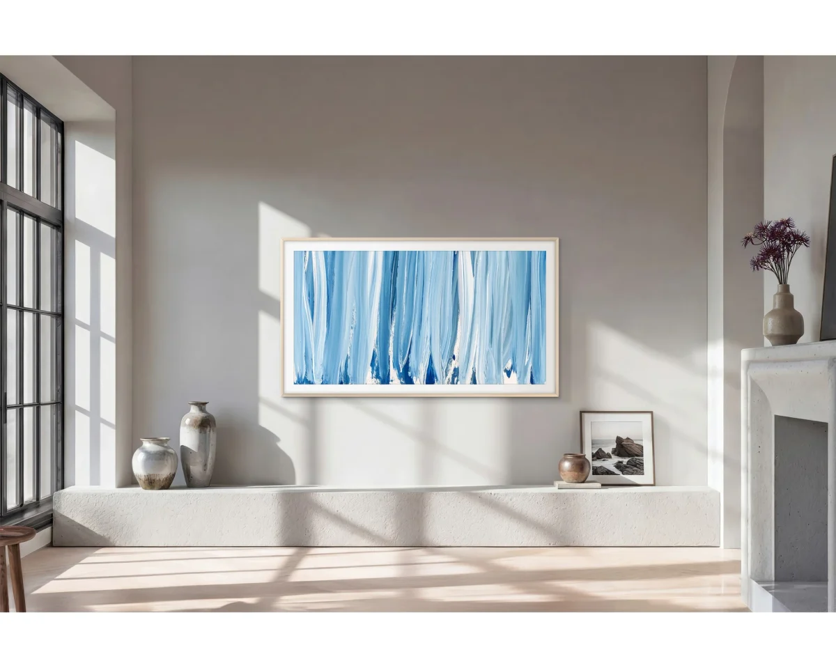 Samsung The Frame Pro 75 polegadas: Sala clara com moldura horizontal na parede exibindo pintura azul, ao lado de vasos, uma foto e uma lareira de pedra.