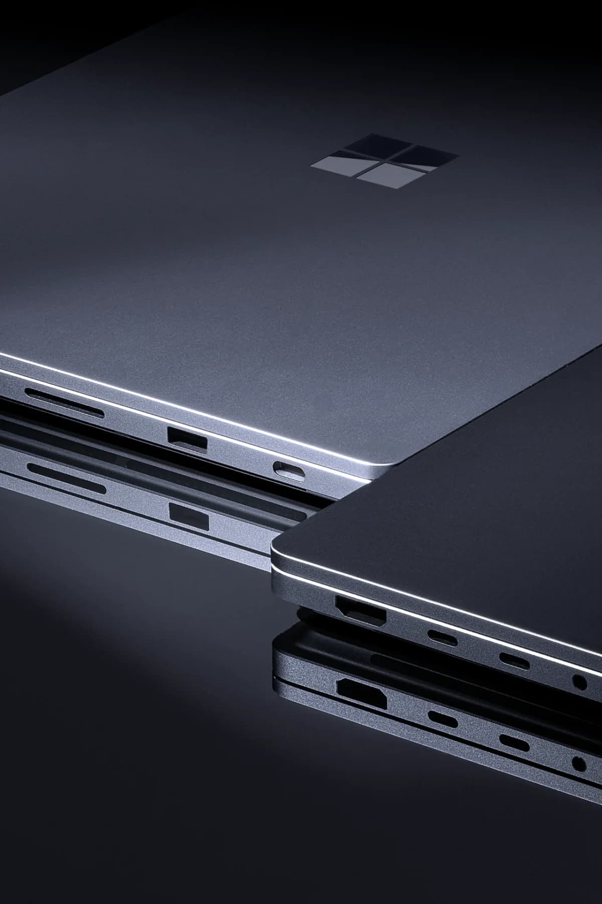 Microsoft Surface Laptop Ultra: Detalhe de dois notebooks escuros fechados, com logotipo da Microsoft na tampa e portas laterais, em superfície reflexiva