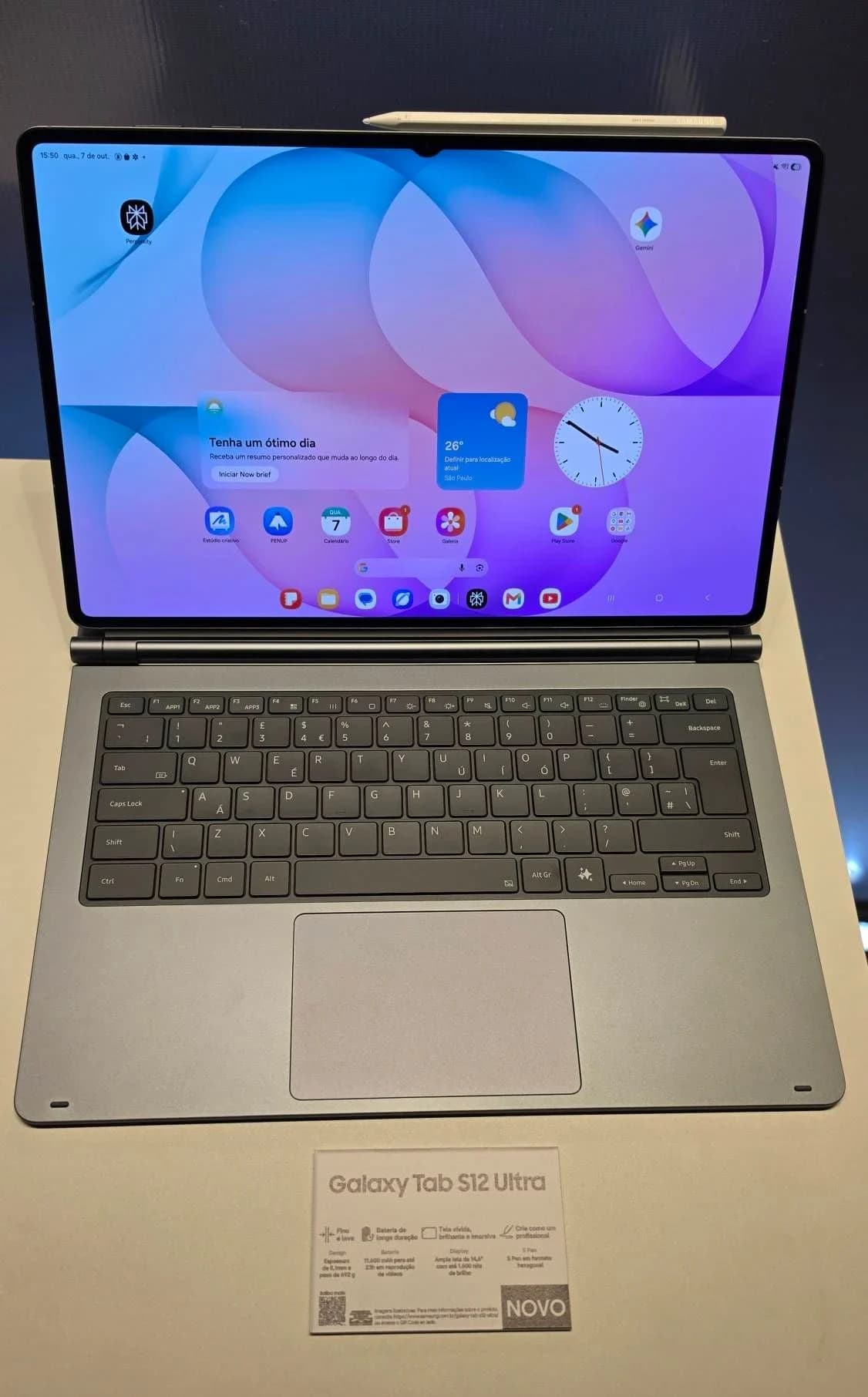 Samsung Galaxy Tab S12 Ultra: Tablet com teclado destacável cinza-escuro sobre a mesa, tela mostrando a página inicial com widgets, caneta encaixada no topo; pl